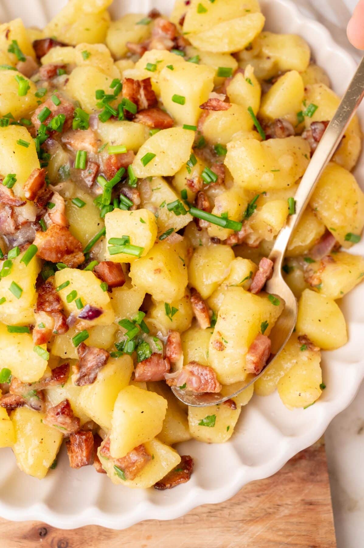 German potato salad topped with bacon and chives in a beige bowl.