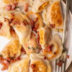 Pumpkin pierogi topped with crispy guanciale on a beige plate.