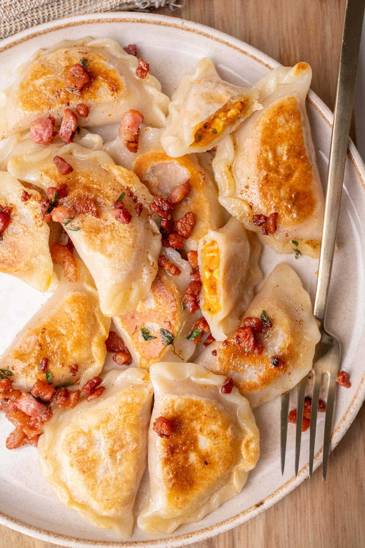 Pumpkin pierogi topped with crispy guanciale on a beige plate.