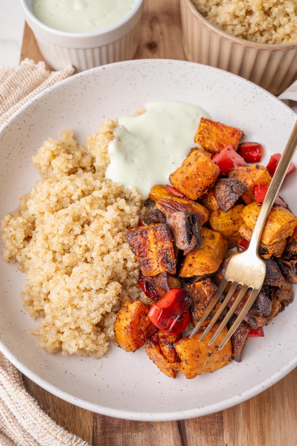 Sweet potatos with bell pepper and mushrooms, served with quinoa and yogurt sauce on a white plate.