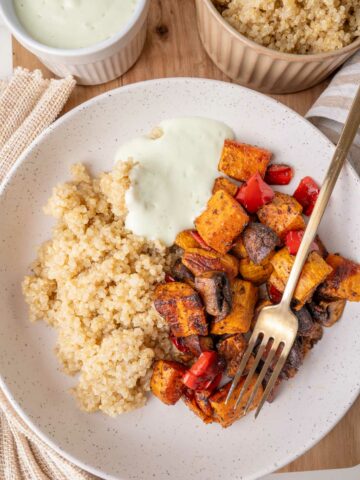 Sweet potatos with bell pepper and mushrooms, served with quinoa and yogurt sauce on a white plate.