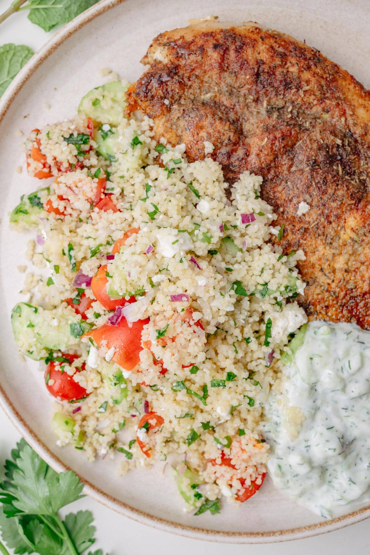 Couscous salad with pan-fried chicken and tzatziki dip on a beige plate.